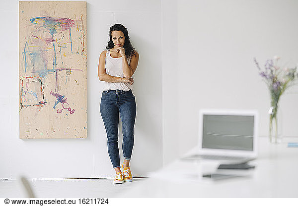 Smiling mid adult woman standing by painting against wall at home