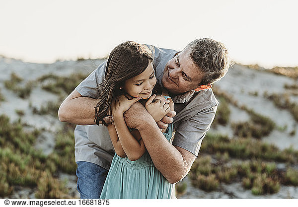 Smiling mid-40's dad hugging young daughter near sand dune