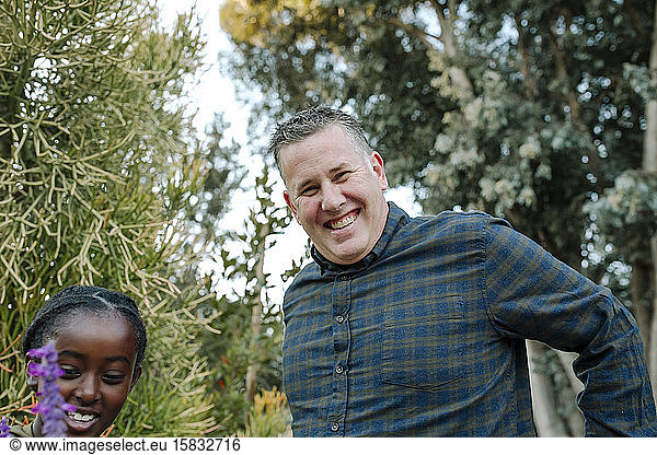 Smiling mid-40's dad in plaid shirt outdoors with black daughter