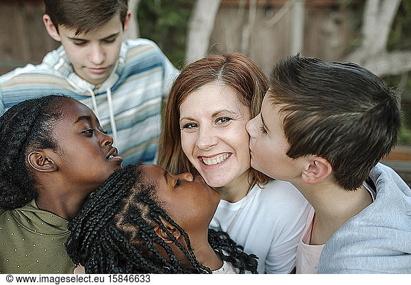 Smiling mid-40's mom being hugged and kissed by multiracial children