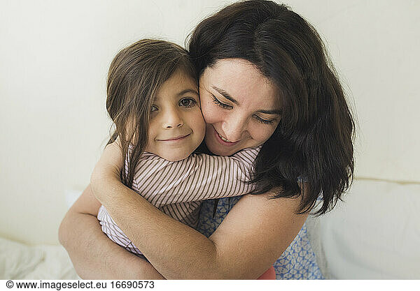 Smiling mid-30's mother hugging happy 6 yr old daughter