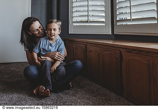 Smiling mom and son sitting on carpeted floor next to window