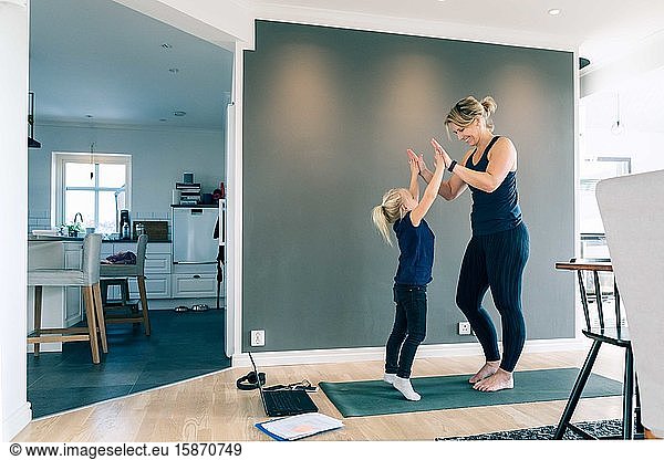 Smiling mother and daughter giving high-five while standing on mat in living room