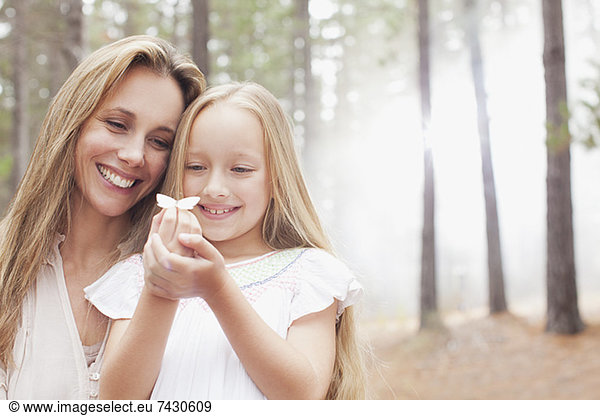 Smiling mother and daughter holding butterfly in woods