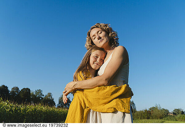 Smiling mother and daughter hugging each other under blue sky