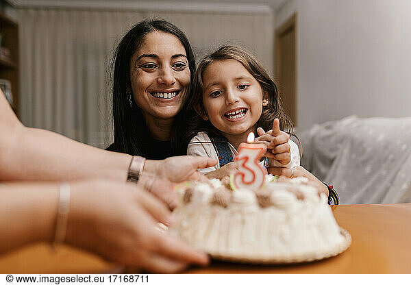 Smiling mother and daughter looking at birthday cake on table at home