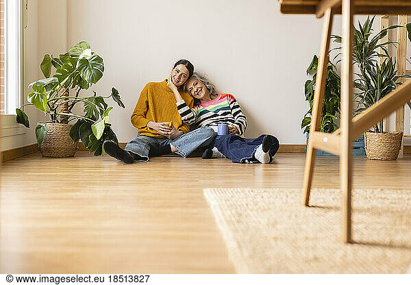 Smiling mother and daughter sitting on hardwood floor at home