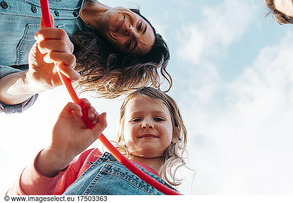 Smiling mother and daughter with hula hoop in front of sky
