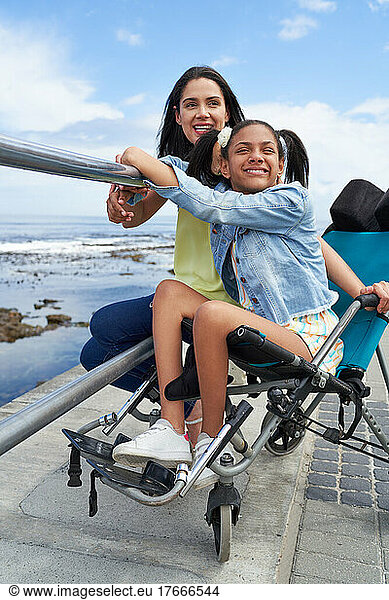 Smiling mother and disabled daughter in pushchair at beach railing