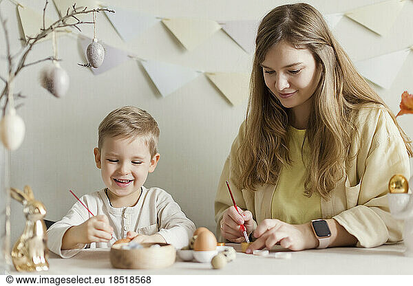 Smiling mother and son decorating Easter eggs at home
