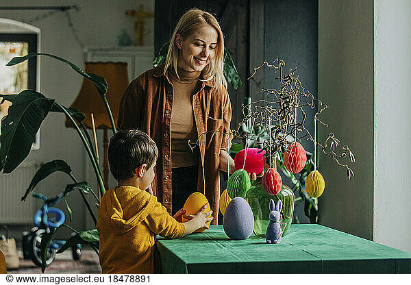 Smiling mother and son decorating table for Easter dinner at home