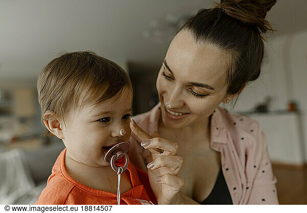 Smiling mother applying cream on nose of daughter at home