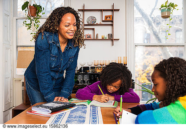Smiling mother assisting daughters in studies at home