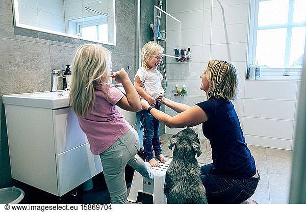 Smiling mother bonding while kneeling in bathroom by dog at home