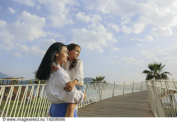 Smiling mother carrying daughter on bridge