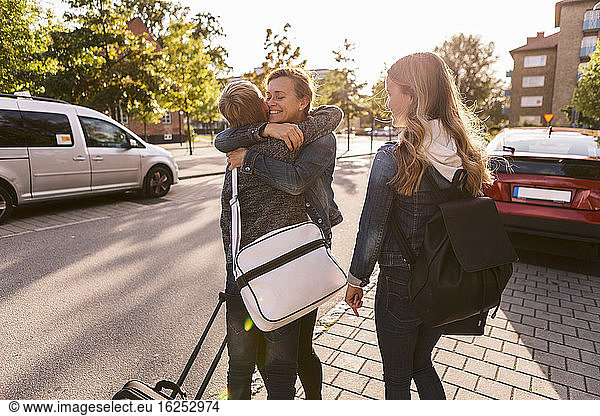 Smiling mother embracing son while daughter standing at roadside