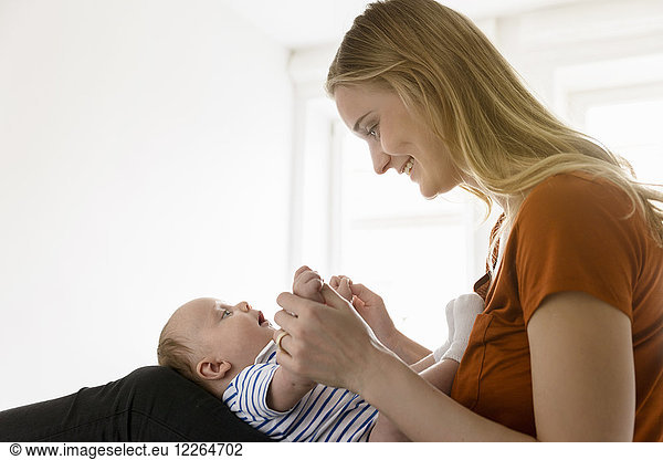 Smiling mother holding baby boy in lap on bed