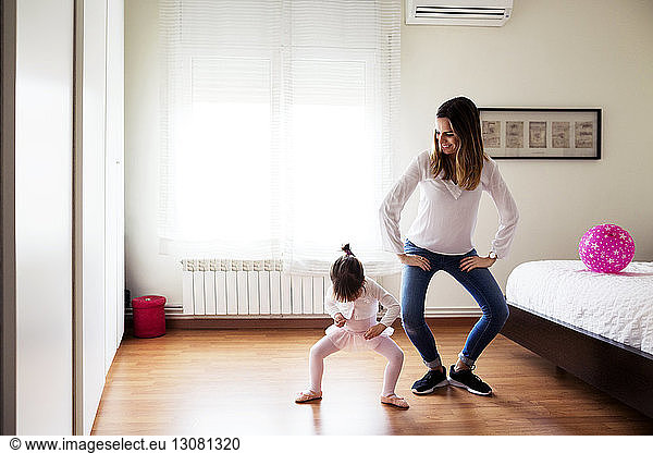Smiling mother imitating girl performing ballet dance in bedroom