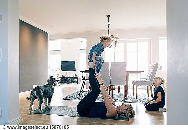 Smiling mother lifting happy daughter while lying on exercise mat at home