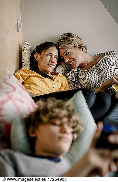 Smiling mother looking at daughter while lying on bed at home