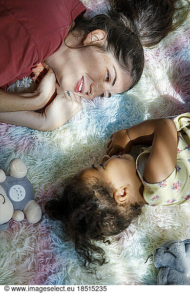 Smiling mother lying on rug with daughter at home