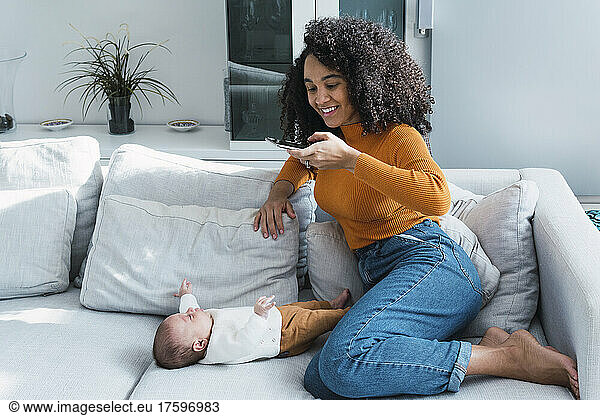 Smiling mother photographing son through mobile phone in living room