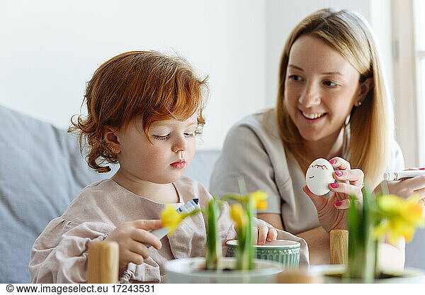 Smiling mother showing Easter egg to daughter at home
