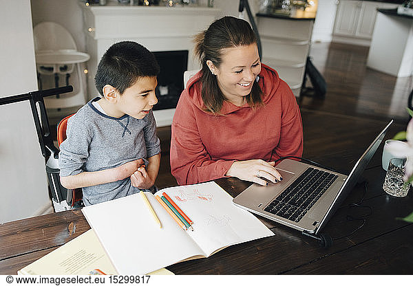 Smiling mother showing video to autistic son on laptop at home