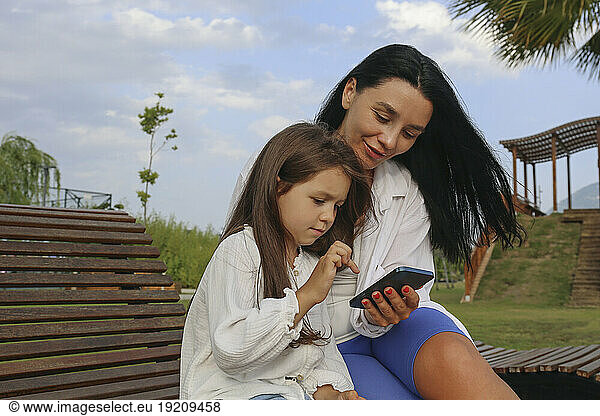 Smiling mother with daughter using smart phone in park