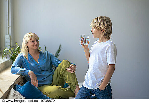 Smiling mother with son holding glass of water at home