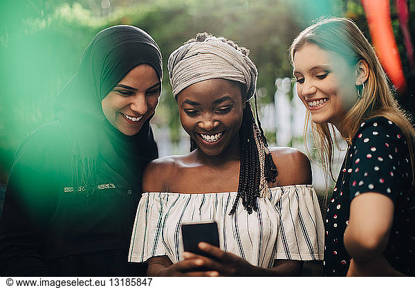 Smiling multi-ethnic female friends looking at mobile phone while standing in backyard
