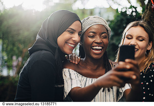 Smiling multi-ethnic female friends taking selfie through mobile phone in backyard