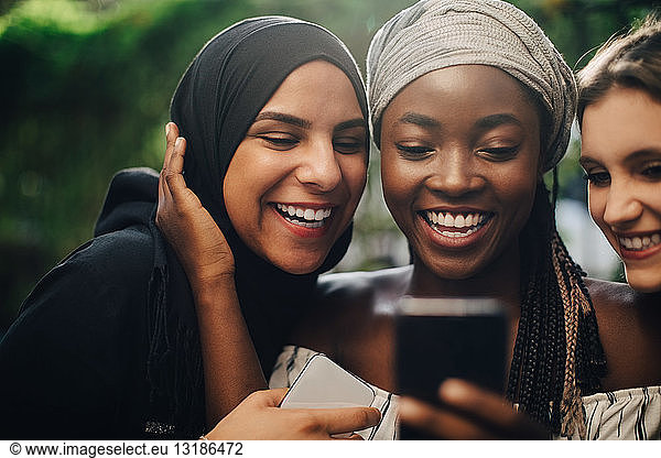 Smiling multi-ethnic friends looking at mobile phone while standing in backyard