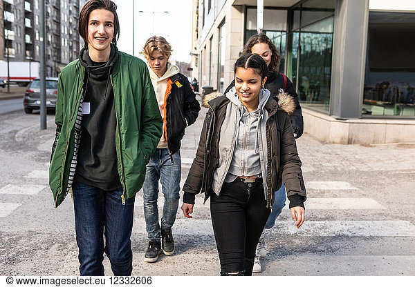 Smiling multi-ethnic teenagers crossing street in city