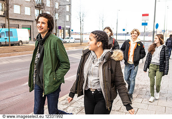 Smiling multi-ethnic teenagers wearing warm clothing walking on sidewalk in city