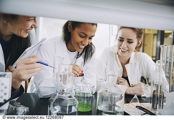 Smiling multi-ethnic university students with mature teacher mixing solution in laboratory
