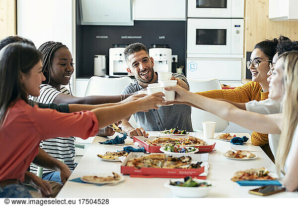 Smiling multiracial colleagues toasting drinks at cafeteria in lunch break