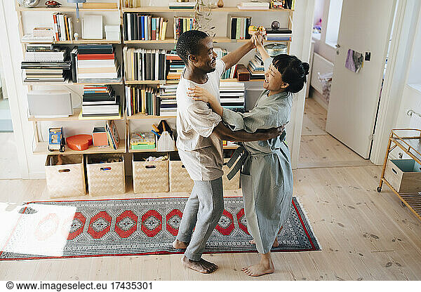 Smiling multiracial couple dancing together in living room at home