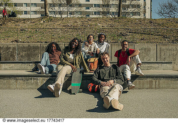 Smiling multiracial male and female friends sitting together at park on sunny day