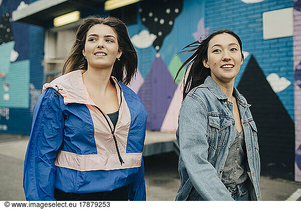 Smiling multiracial young women looking away while walking on street