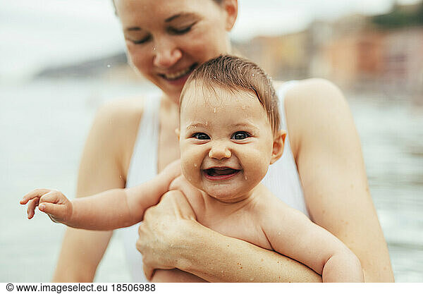 Smiling mum holds happy baby while swimming in Mediterranean