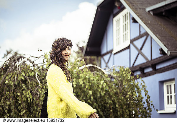 smiling natural girl in yellow jumper walks by blue traditional house
