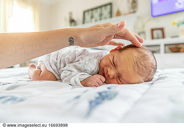Smiling newborn baby laying on stomach as mother gently touches head.