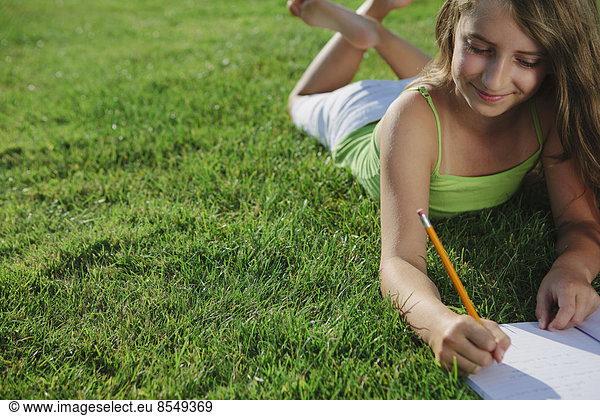 Smiling nine year old girl sitting on grass  writing in notebook