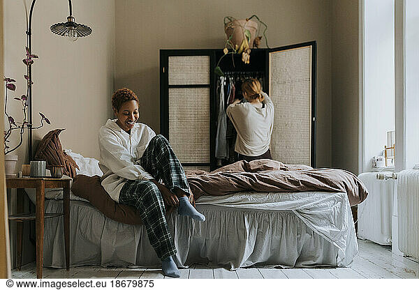 Smiling non-binary person wearing socks while sitting on bed at home