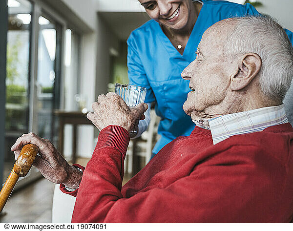 Smiling nurse giving water to senior man at home