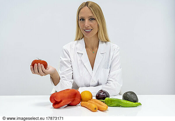 Smiling nutritionist with vegetables sitting at desk in hospital