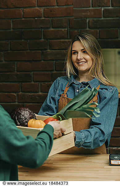 Smiling owner receiving crate of vegetables from delivery person at cafe