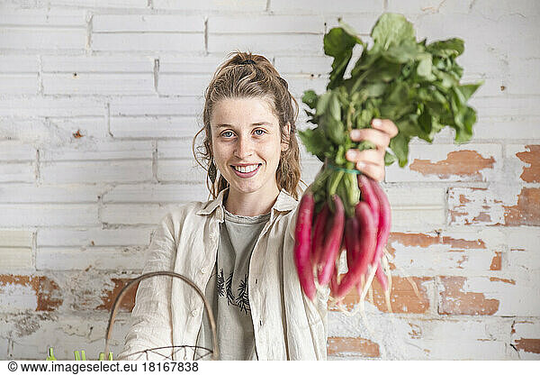 Smiling owner showing fresh radish in front of brick wall
