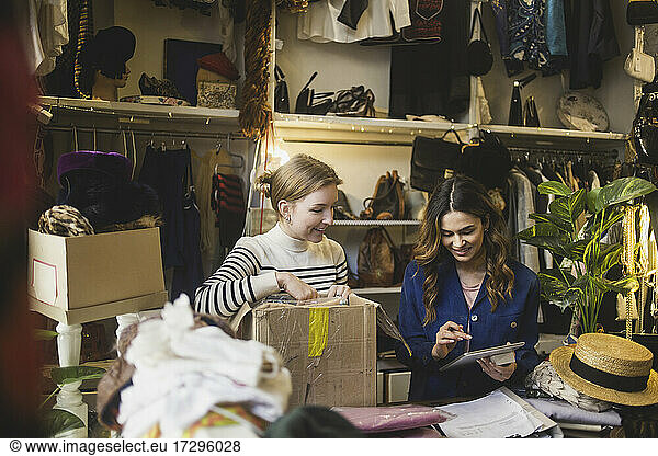 Smiling owner using digital tablet standing by female colleague in boutique